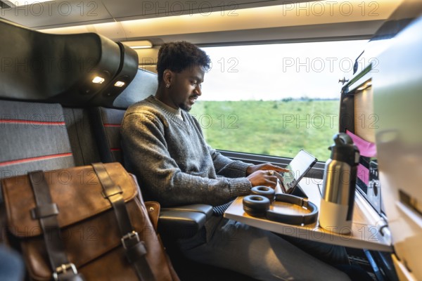 Young african businessman staying productive on a train, working on a tablet with headphones, managing tasks and staying connected while commuting between destinations