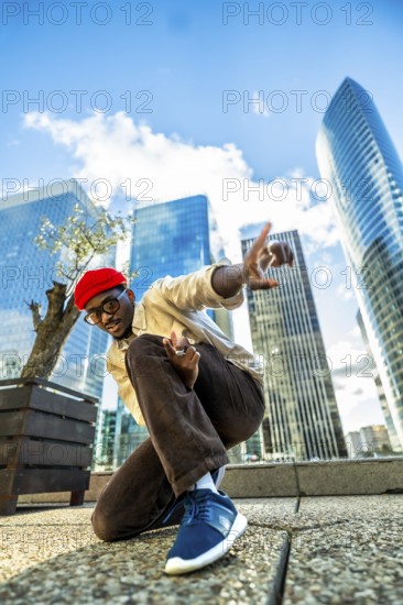 Young black man in a red beret and glasses posing confidently with hands gesturing, expressing urban style and freedom in a modern financial district with skyscrapers under a blue sky