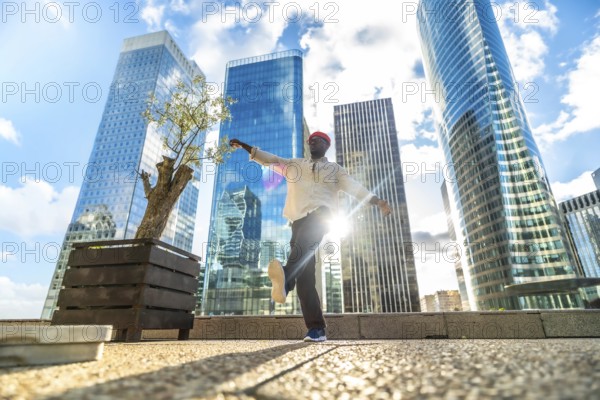 African american man dancing joyfully in a modern city square, arms outstretched against towering glass skyscrapers and blue sky, radiating freedom, energy and confidence