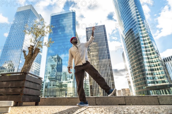 Happy black man celebrating joy and freedom with a dynamic dance on a urban plaza, surrounded by towering contemporary skyscrapers under a blue sky, symbolizing success and aspiration