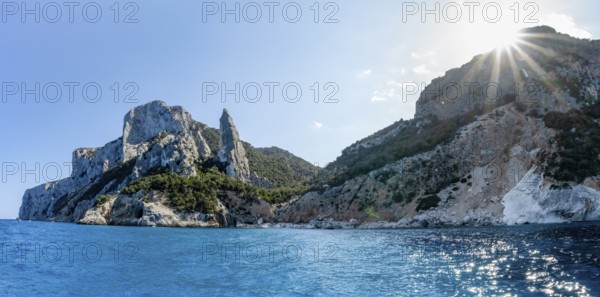 Light blue clear sea on a dream beach on Cala GoloritzÃ©, picturesque rocky coast with sun stars, cliffs with rock peak L'Aguglia, Golfo di Orosei, Baunei, Sardinia, Italy
