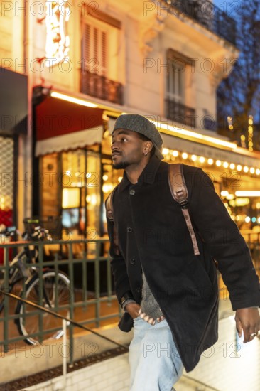 Young black man wearing a beret, coat, and backpack exploring the brightly lit streets of paris, france, at night, symbolizing travel, urban lifestyle, and fashion