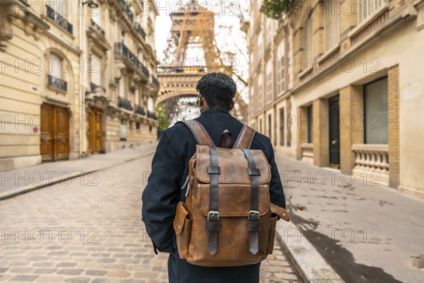 Male tourist wearing a backpack walking on a cobblestone street in paris, experiencing travel and discovering the urban cityscape with the iconic eiffel tower in the distance