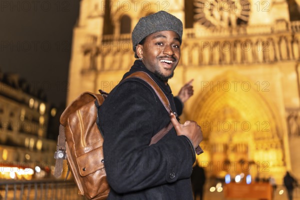 Young african american man smiling and pointing, enjoying a night out in paris and exploring an illuminated historic building during his trip to france