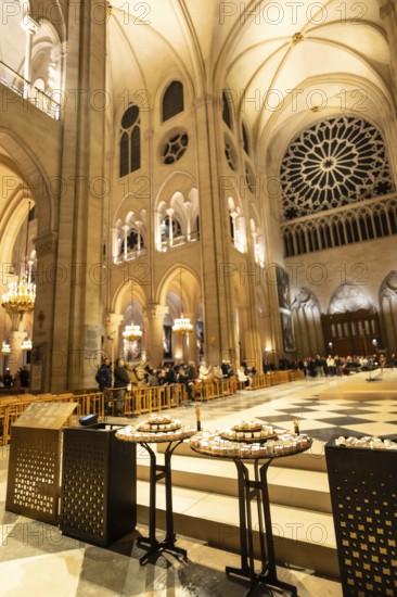 Notre dame cathedral interior in paris, france, displaying intricate gothic architecture, vaulted ceilings, a large rose window, and people gathering during an event with votive candles