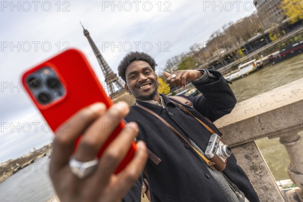 Young black man smiling and taking a selfie with a smartphone, capturing a memorable travel moment in paris overlooking the city with the eiffel tower in the background