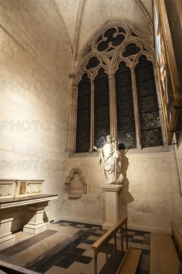 Gothic chapel interior featuring a statue of a saint, an arched window with detailed tracery, and checkered floor, highlighting the rich religious history and architectural beauty