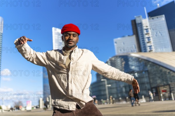 Young black man showing movement and expressing himself through dance in an urban setting with modern skyscrapers and architecture under a clear blue sky