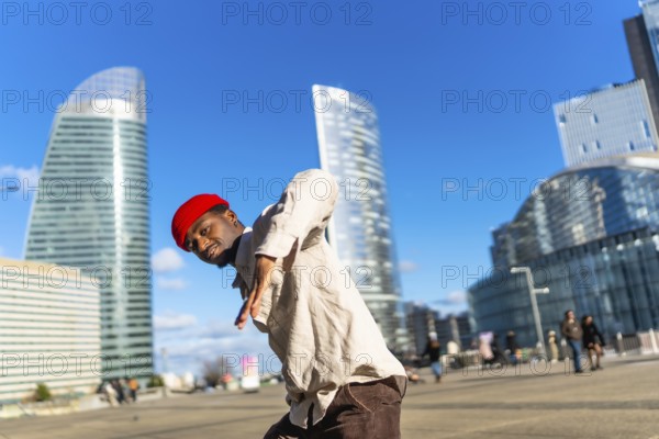 Young black man performing dynamic street dance in la defense, paris, striking a confident pose against sunlit contemporary skyscrapers and a bright blue sky