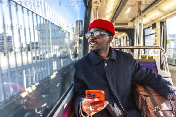 African man passenger traveling by tram, looking out the window while holding a mobile phone, representing urban transport, daily commute, and modern city life