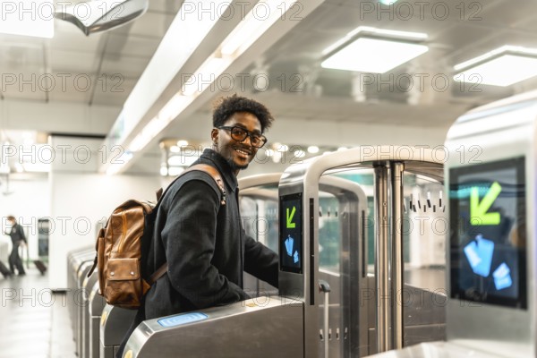 Young african american man with a backpack smiling, entering through a modern turnstile at a metro station, using public transport for his daily commute or travel
