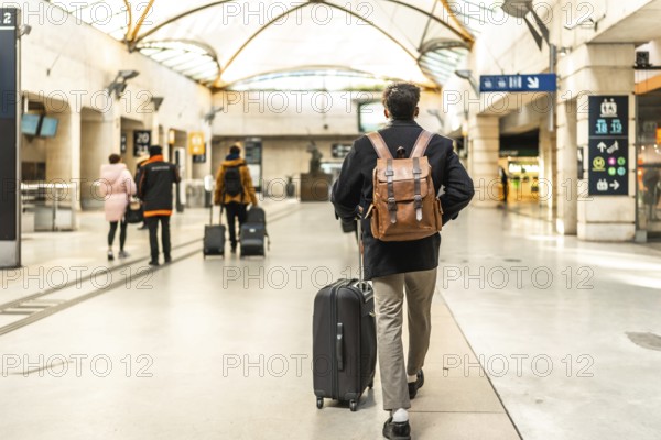Businessman walking through a modern train station, pulling a suitcase and wearing a backpack, highlighting concepts of travel, commuting, business trips, and transportation