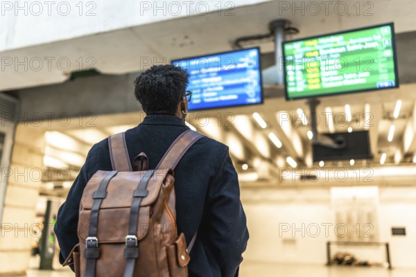 Man with a backpack standing at a train station, looking at the departure boards, preparing for a journey or business travel while waiting for his connection