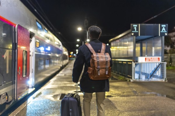 Man in coat and backpack pulls rolling luggage on a dim train platform at night, boarding for a business trip lone urban traveler heading into the city for work and adventure