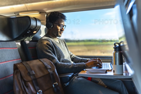 Young professional with headphones and glasses focused on laptop, working efficiently on a high speed intercity train, staying connected and productive during travel