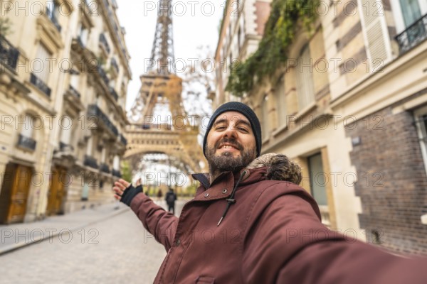 Happy bearded man in winter clothes takes a smiling selfie with the eiffel tower behind him, enjoying a cheerful paris sightseeing stroll and urban travel getaway