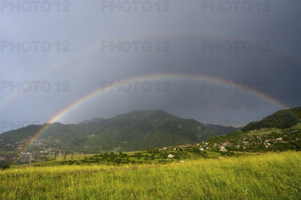 Two rainbows stretch across a green landscape with mountains and a village under a cloudy sky, Lorikeet province, Armenia