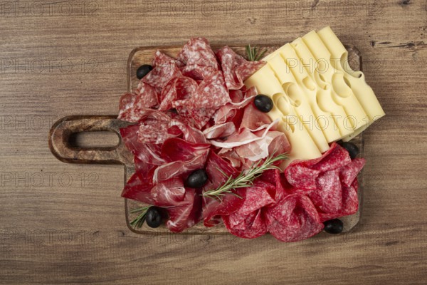 Assorted meat, appetizer, prosciutto, salami and ham, with maasdam cheese and olives, on a wooden board, breakfast, top view, close-up, no people