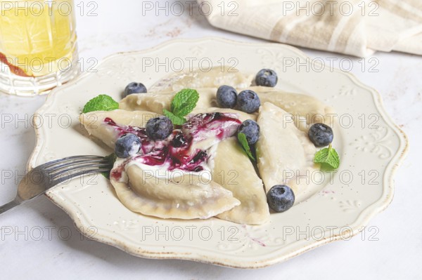 Handmade dumplings filled with sweet ingredients, arranged beautifully on a white plate, topped with berry sauce, fresh blueberries, and mint leaves, ready to enjoy