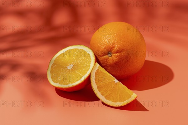 On the coral surface, next to two neatly sliced slices, there is a whole orange. Sunlight casts soft shadows, emphasizing the freshness and bright color of the fruit