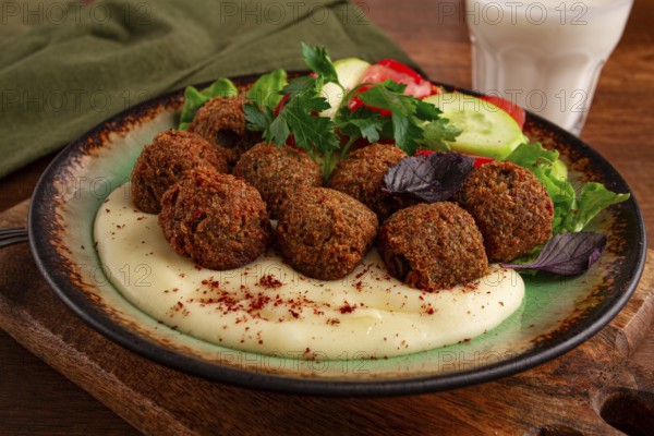 A plate holds falafel balls, tahini, salad with tomatoes and cucumbers, and a drink. The setting is warm and inviting, perfect for a midday meal with fresh ingredients
