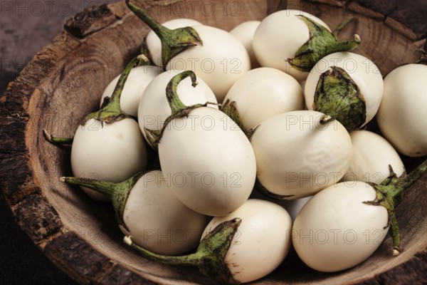 White mini eggplant, in a wooden bowl, on the table, close-up