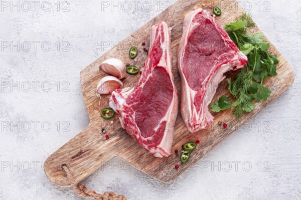 Fresh pieces of beef on the bone, on a wooden cutting board, with herbs and spices, ready for cooking in the kitchen