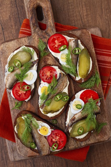 Sandwiches on rye bread with sprats, quail eggs, fresh tomatoes and pickled cucumber, on a wooden board, appetizer, breakfast