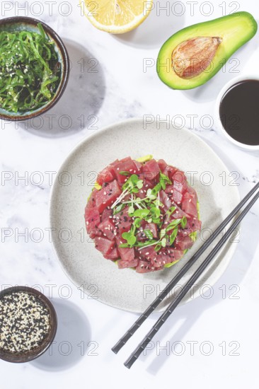 Fresh tuna tartare with avocado served on a marble table with soy sauce and seaweed salad