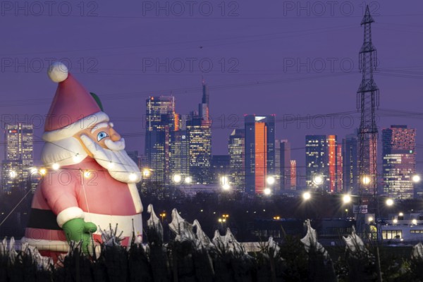 In a Christmas tree center near Frankfurt am Main, a multi-metre-high inflated figure of Santa Claus rises in front of the glowing banking skyline, Frankfurt am Main, Hesse, Germany
