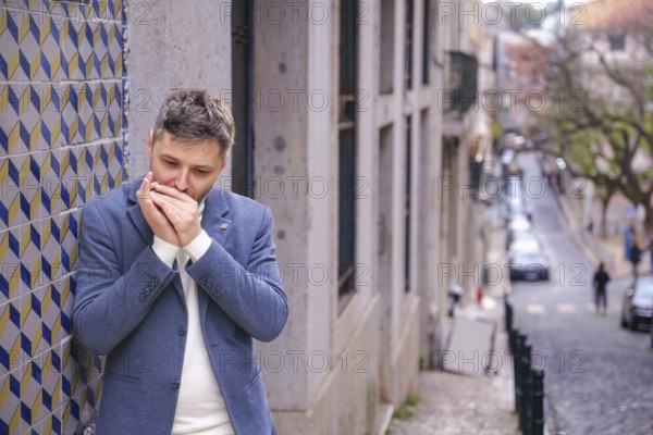Man musician in a blue blazer and white sweater playing blues on a harmonica with eyes closed, standing outdoors in city street