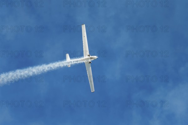 Stunt aerobatic plane performing stunts in blue sky with smoke trail. Concept of speed, difficulty, precision, risk, challenge