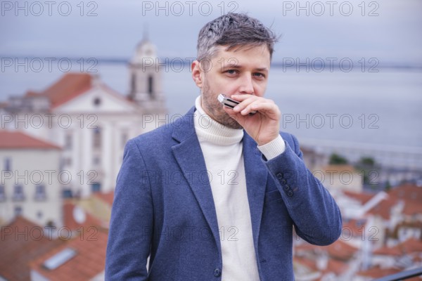 Man musician in a blue blazer and white sweater playing blues on a harmonica with eyes closed, standing outdoors in Lisbon city street, Portugal