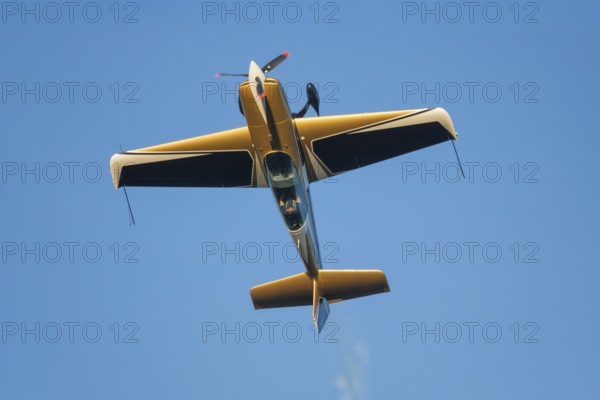Golden stunt aerobatic plane performing stunts in blue sky. Concept of speed, difficulty, precision, risk