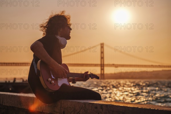 Hipster street musician in black playing electric guitar in the street on sunset