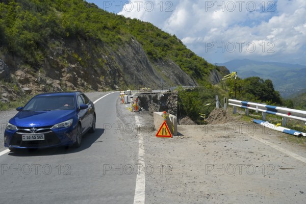 A car drives along a winding mountain road, next to a construction site and lush green areas, road has slipped down, Debed gorge, Lorikeet province, Armenia