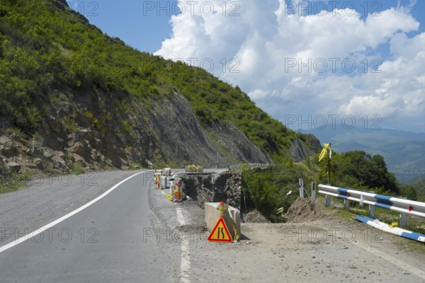 A winding mountain road with a construction site, surrounded by green hills and cloudy sky, road has slipped down, Debed gorge, Lorikeet province, Armenia