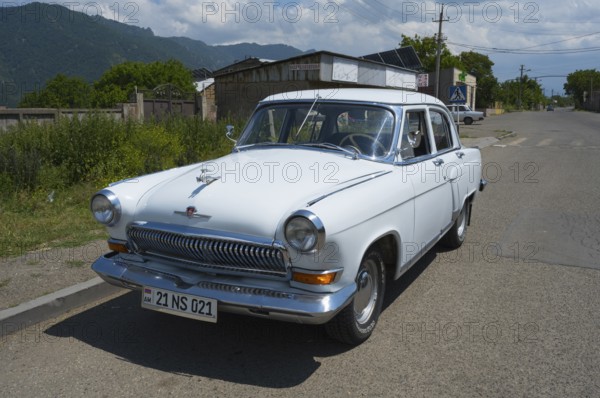 White vintage car on a country road with mountain backdrop and blue sky in summer, GAZ M-21 Volga, Odsun, Odzun, Debed Gorge, Lorikeet Province, Armenia