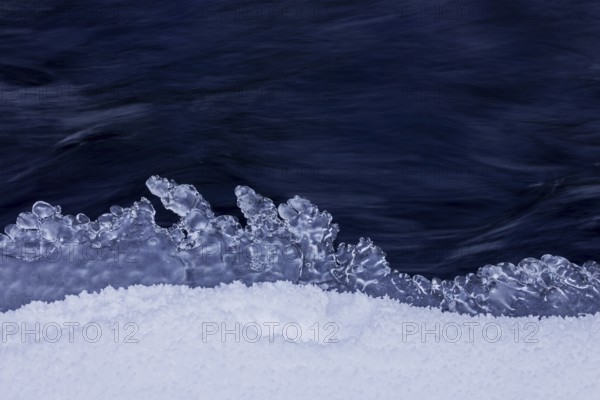 Ice formation formed by frost and freezing cold temperatures over running water of stream along riverbank / river bank in winter