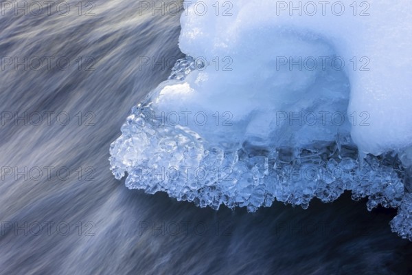 Ice formations and icicles formed by frost and freezing cold temperatures over running water of stream along riverbank / river bank in winter