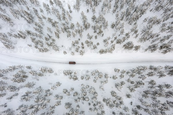 Aerial view over car, van driving over snow covered road through the taiga in winter, Riisitunturi National Park, Lapland, Posio, Koillismaa, Finland
