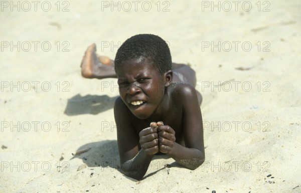 Local boy lying in the sand at Kande Beach on Lake Malawi and smiling at the camera, Malawi, Africa, July 2000, vintage, retro, old, historic