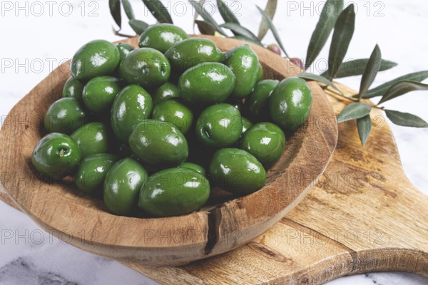 Halkidiki olives, classic Greek green olives, in a wooden bowl, on a cutting board, top view, without people