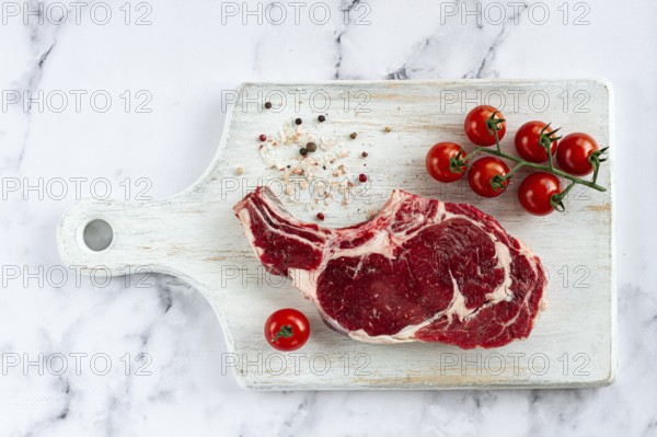 Raw rib eye steak, cowboy steak, on a white wooden chopping board, marble table, top view, no people
