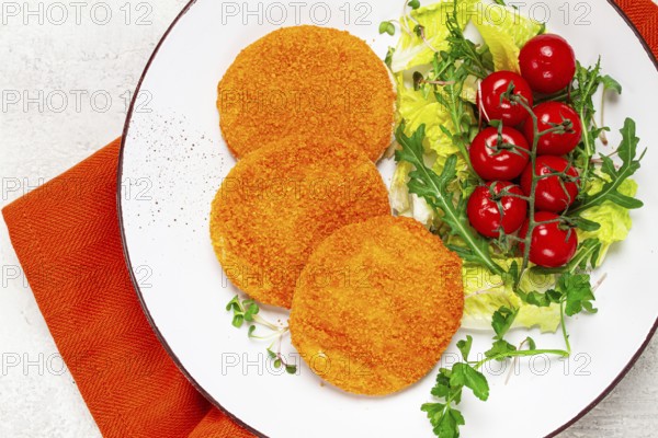 Crispy fried fish cutlets, fish burgers, on a white plate, with fresh lettuce leaves, arugula and cherry tomatoes, homemade, no people