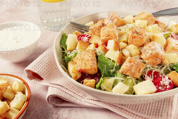 Caesar salad with salmon, with croutons and dressing, in a salad bowl, on a pink table