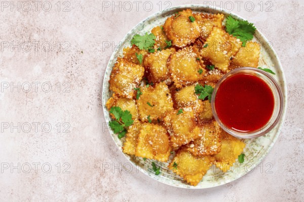 Fried ravioli with parmesan cheese, served with red sauce and garnished with herbs, on a light background, no people