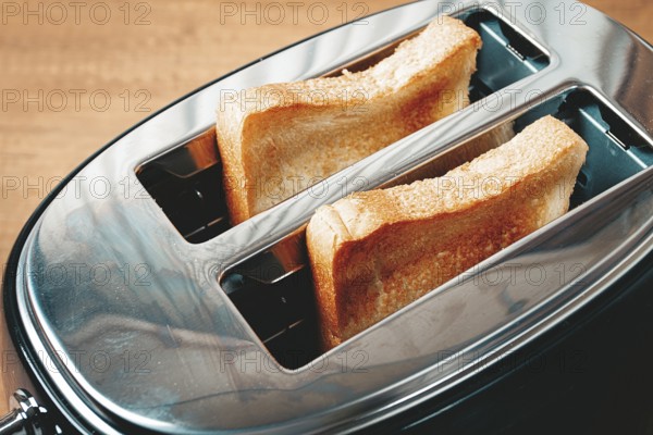 Two slices of bread are toasting in a shiny metal toaster, set on a countertop in a warm kitchen. The soft light suggests a cozy breakfast atmosphere