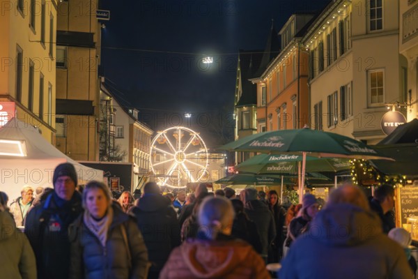 A Ferris wheel in the distance illuminates a busy street of a Christmas market, Christmas market 2025, Nagold, Black Forest, Calw district, Germany