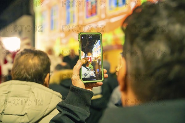 People watch a colorful event, with some capturing the scene with smartphones, Christmas market 2025, Nagold, Black Forest, Calw district, Germany
